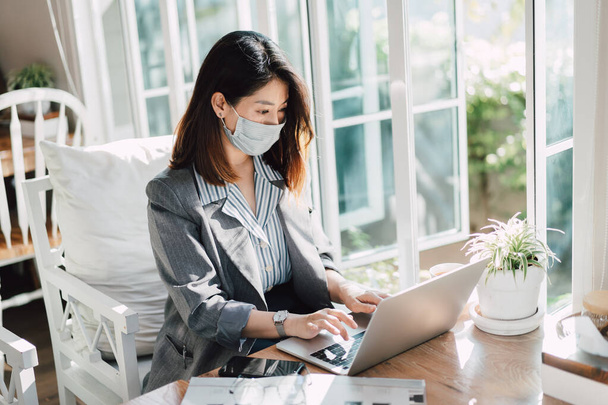 business women wearing surgical mask and using laptop on the table in the cafe - Foto, afbeelding