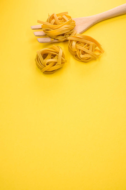 A vertical shot of tagliatelle pasta and a wooden kitchen tool - Fotografie, Obrázek
