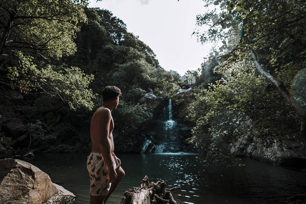 Een jonge blanke man heeft het naar zijn zin bij een prachtige waterval bij rotsen - Foto, afbeelding