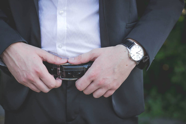 A closeup shot of a male in a suit holding his belt - Fotó, kép