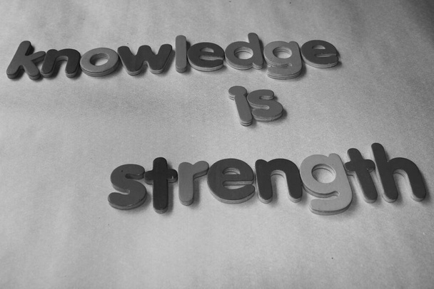Wissen ist Stärke. Wissen ist Stärke, die mit dem hölzernen englischen Alphabet an die Wand geschrieben wird. - Foto, Bild