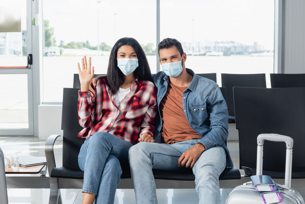 african american woman waving hand near man in medical mask near luggage in departure lounge  - Foto, Imagem