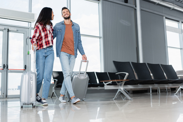 alegre casal multicultural andando com bagagem no aeroporto  - Foto, Imagem