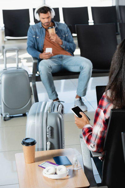 vista posterior de la mujer sosteniendo teléfono inteligente con pantalla en blanco cerca del equipaje y el hombre sobre fondo borroso  - Foto, Imagen