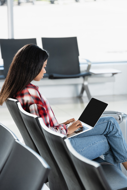 brunette african american woman using laptop in departure lounge of airport - Photo, Image