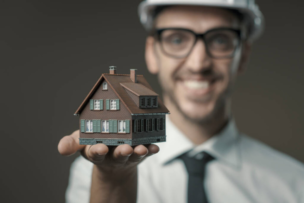 Smiling architect holding a model house, real estate and construction industry concept - Photo, Image