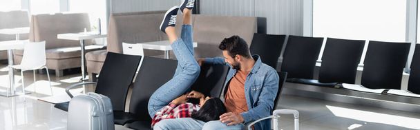 afro-américaine avec les jambes levées couché près de l'homme dans le salon de départ de l'aéroport, bannière - Photo, image