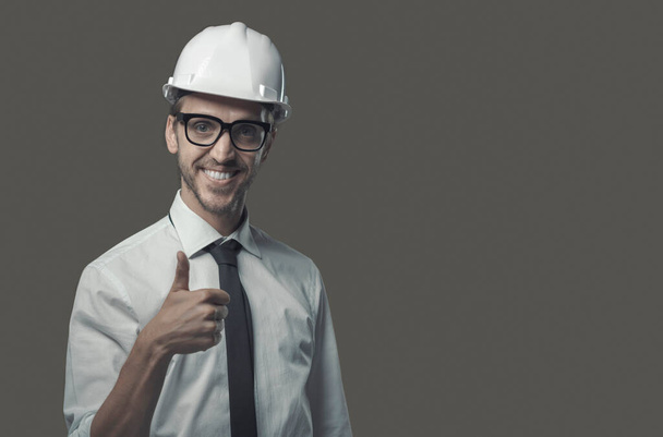 Smiling confident architect wearing a safety helmet and giving a thumbs up - Photo, image