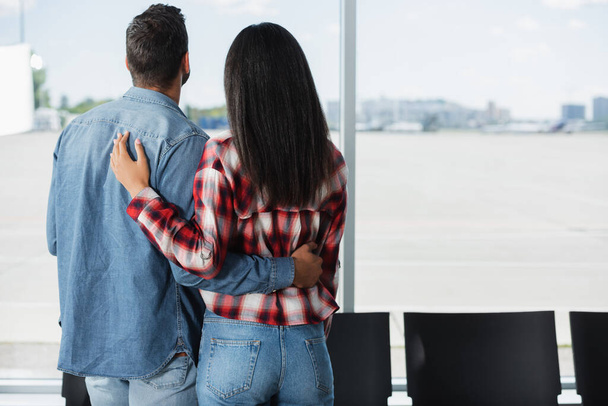 back view of interracial couple standing in departure lounge of airport - Φωτογραφία, εικόνα