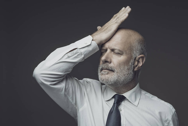 Disappointed businessman touching his forehead, he has made a mistake and feels regretful - Foto, afbeelding