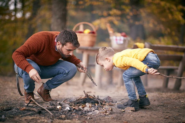 Père et fils soufflant pour allumer le feu de camp dans la forêt par une belle journée d'automne - Photo, image