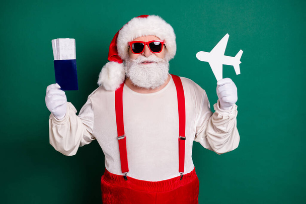Portrait of his he handsome bearded cheerful funky fat overweight Santa father holding in hand paper plane shape ticket document tour resort destination first class isolated green color background - Foto, imagen