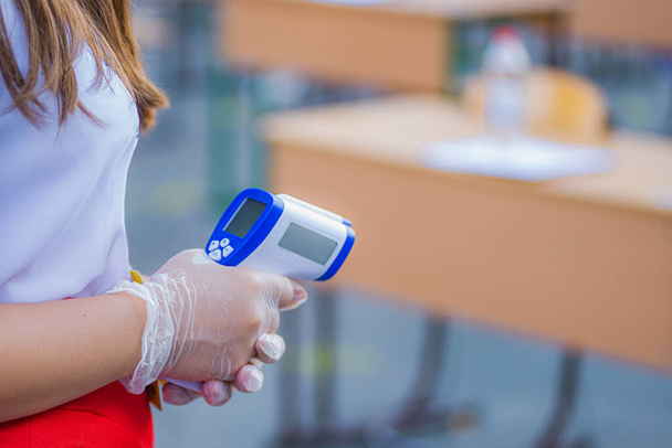 Dívka v rukavicích drží elektronický teploměr, který kontroluje teplotu. Regulace teploty, aby se zabránilo šíření koronaviru. - Fotografie, Obrázek