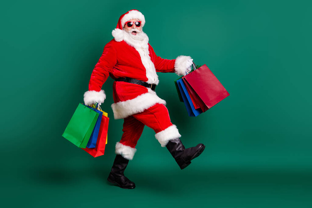 Full length body size profile side view of his he nice fat overweight cheerful glad Santa carrying bags Eve Noel gifts presents surprise festive newyear tradition isolated over green color background - Φωτογραφία, εικόνα