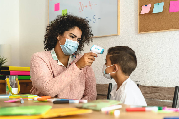 Καθηγήτρια γυναίκα θερμοκρασία ελέγχου για το παιδί στην τάξη κατά τη διάρκεια της πανδημίας του ιού του στέμματος - Υγεία ιατρική και εκπαίδευση έννοια - Φωτογραφία, εικόνα