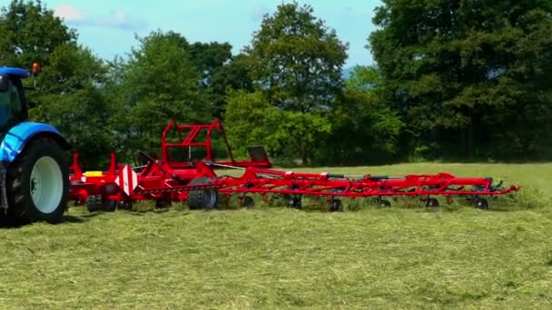 Een tractor rijdt over het veld en bereidt hooi voor. Roterende harken op de landbouwmachines bewegen zeer snel en draaien hooi om. - Video