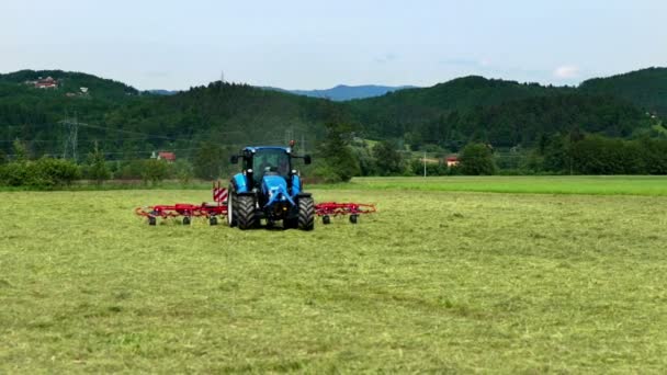 Een boer die in een tractor zit, werkt hard en bereidt in de zomer hooi voor. De roterende harken bewegen snel.. - Video