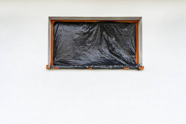 Une couche nouvellement appliquée de plâtre de silicone blanc sur le mur de la maison, la fenêtre est fixée avec du papier d'aluminium noir. - Photo, image