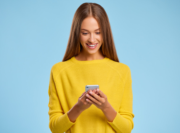 funny cheerful woman in a yellow sweater with smartphone on colored yellow backgroun - Fotó, kép