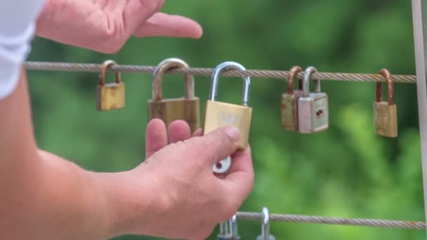 男が橋の上のワイヤーに鍵をかけている。これはカップルの無限の愛の兆候です。. - 映像、動画