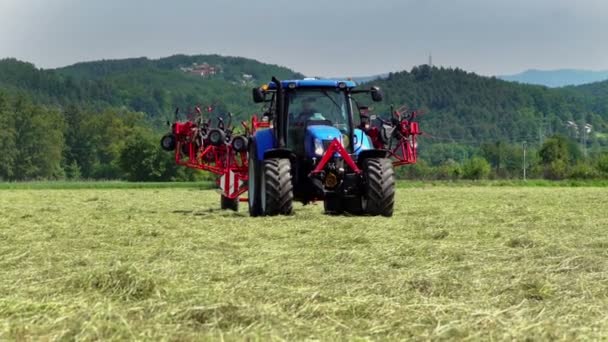 Modrý traktor pomalu projíždí velkým polem a zemědělské stroje se skládají dohromady. V pozadí jsou kopce.. - Záběry, video
