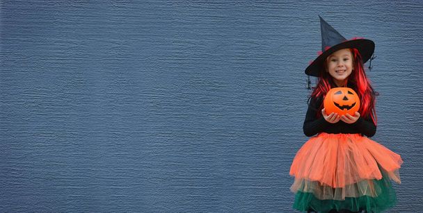 Dolcetto o scherzetto di Halloween. Ritratto ragazza sorridente con cappello da strega contro un muro blu. Copia spazio per testo - Foto, immagini