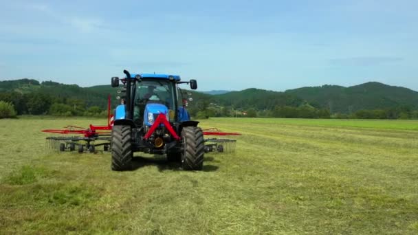 Modrý traktor je připojen k velkému strojnímu zařízení pro přípravu sena. Farmář má práci venku.. - Záběry, video