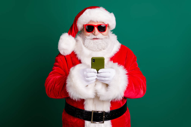 Photo of retired stylish grandpa white beard hold telephone chatting snow-maiden forget presents wear red santa x-mas costume coat gloves sunglass headwear isolated green color background - Photo, Image