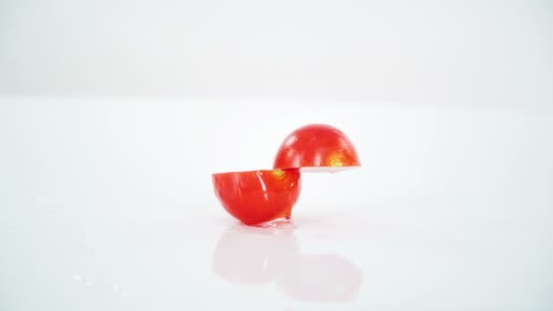 Un tomate cortado en dos mitades cae sobre la mesa. Luego se divide. Allí también hay agua en la mesa.. - Metraje, vídeo