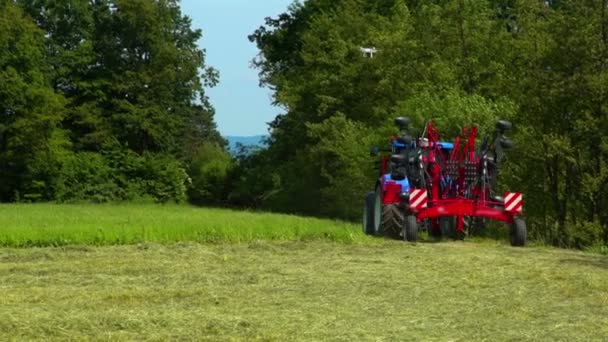 Een tractor trekt er een landbouwmachine achter aan en hij rijdt een bos in. Hij is klaar met het bereiden van hooi.. - Video