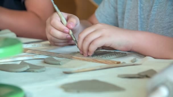 I bambini della scuola stanno usando diversi strumenti e spazzole quando stanno facendo qualcosa di argilla nella loro classe di arte. - Filmati, video