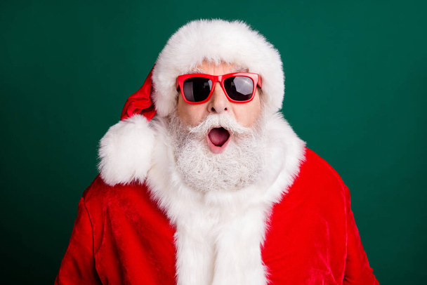 Closeup headshot photo of pensioner old man grey beard open mouth surprised see another man same outwear wear red santa costume coat sun glasses headwear isolated green color background - Fotografie, Obrázek