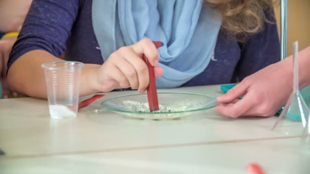 Een meisje voert een experiment uit tijdens een scheikundeles. Ze heeft een gereedschap in haar hand en een speciale substantie op een bord.. - Video