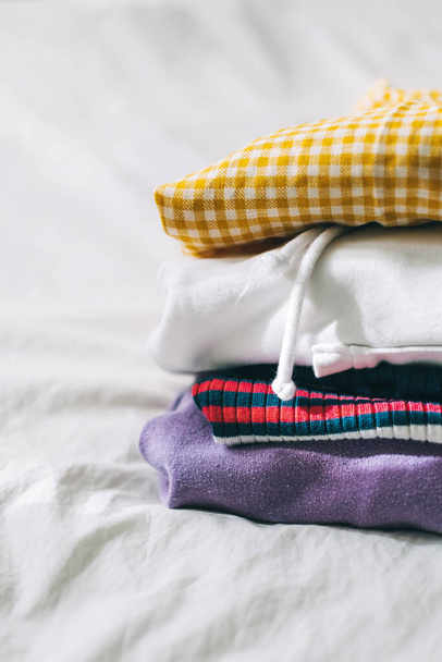 Stack of multicolored clothes on a white bed from wardrobe. High quality photo - Foto, Imagen