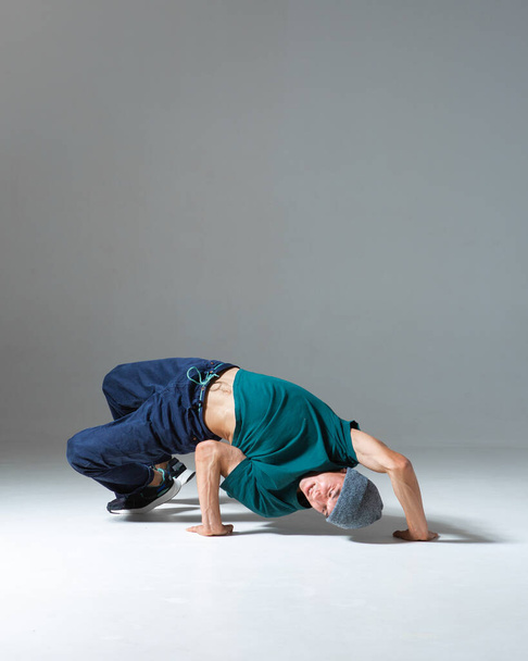 Young guy breakdancer dancing lower break dance isolated on gray background. Break dance lessons - Photo, Image