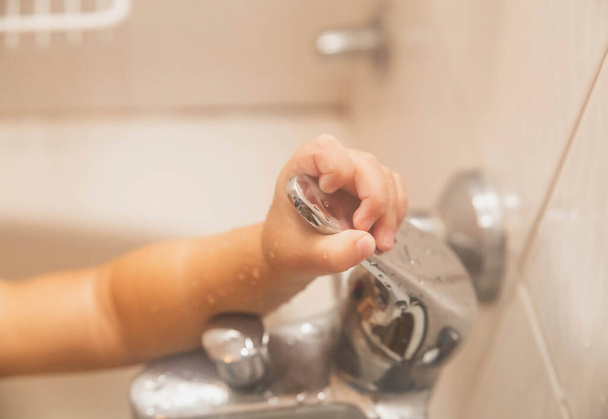 Bebek banyoda yıkanır, musluğa tutunur. - Fotoğraf, Görsel