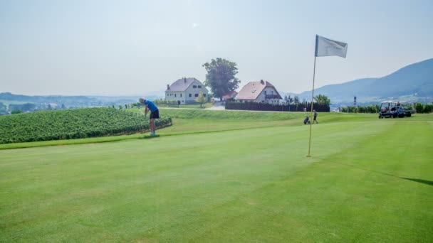 Una pelota de golf se detiene justo antes de llegar a una bandera. Una mujer de mediana edad está jugando golf. El día es agradable y soleado. - Imágenes, Vídeo