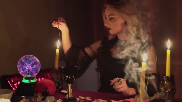 Mulher cartomante segurando um pêndulo mágico sobre a vela e depois sobre a foto - Filmagem, Vídeo