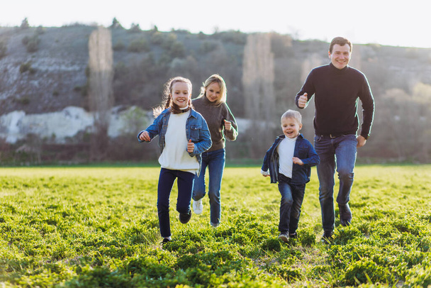 Father, mother and children run through a green field. - Photo, Image