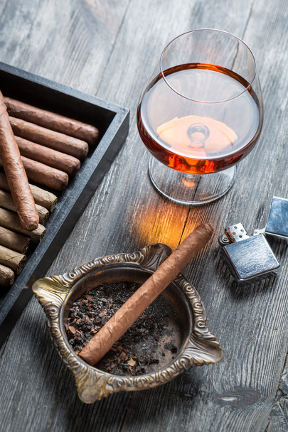Cigar in ashtray, lighter and cognac - Foto, afbeelding