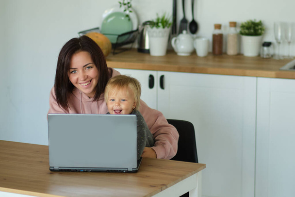 Trabajando desde casa con un niño. Madre e hija usando laptop e Internet. Trabajo freelancer. Mujer feliz enseñando a un niño pequeño. Enseñanza a distancia, aislamiento, educación en el hogar. Momento de estilo de vida - Foto, Imagen