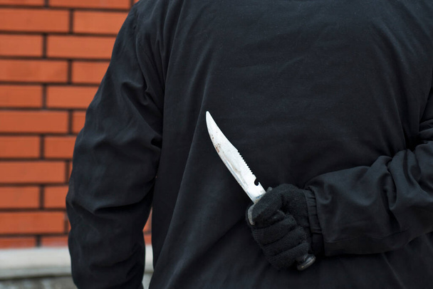 Ο άνθρωπος με το μαχαίρι πίσω από την πλάτη του. Ένας άντρας κρατάει κοφτερό μαχαίρι πίσω από την πλάτη του. - Φωτογραφία, εικόνα