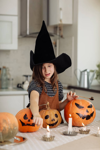 Feliz Halloween. Linda niña en traje de bruja con calabaza tallada. Familia feliz preparándose para Halloween. niña enciende velas. - Foto, imagen