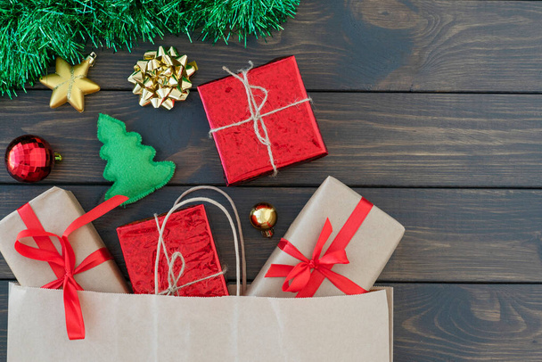 ploché ležely malé dárkové krabičky unavené stuhou, novoroční věcmi, zeleným cínem na dřevěném pozadí, kopírovacím prostorem pro text. Nový rok nakupování. Vánoční a novoroční koncept - Fotografie, Obrázek