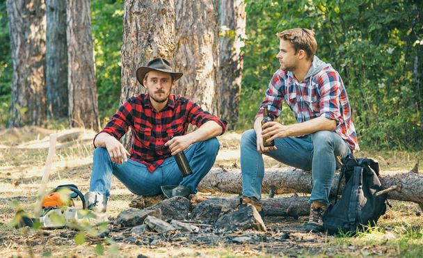 Friends spend leisure weekend forest nature background. Two Happy people sitting around campfire with beer. Friends enjoy weekend camp in forest. Summer lifestyle. - Fotó, kép