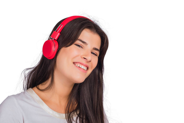Portrait of young beautiful woman listening to music with red headphones on studio. Isolated white background. - Foto, immagini