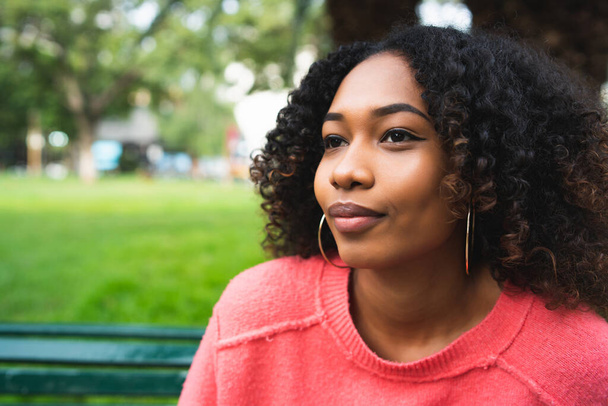 Portrait of young beautiful afro american woman sitting on bench in the park. Outdoors. - 写真・画像