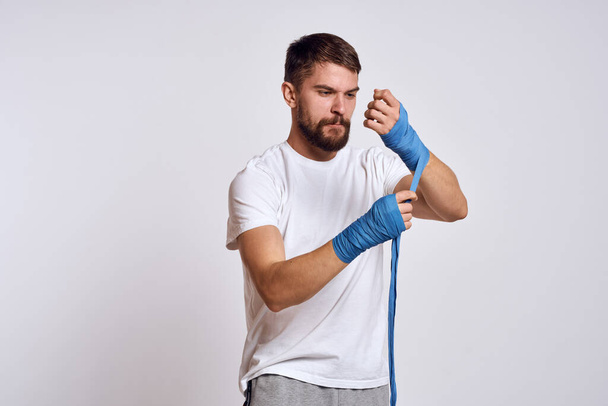 homem de esportes em branco t-shirt azul bandagens de boxe em seus exercícios de treino de braços - Foto, Imagem