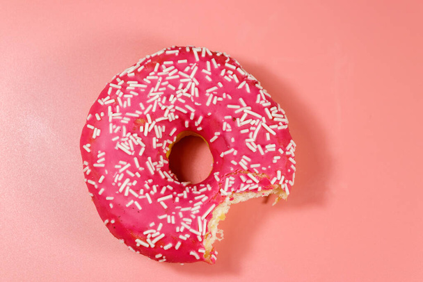 Mordido sabroso rosado donut sobre fondo rosa. Vista superior - Foto, imagen