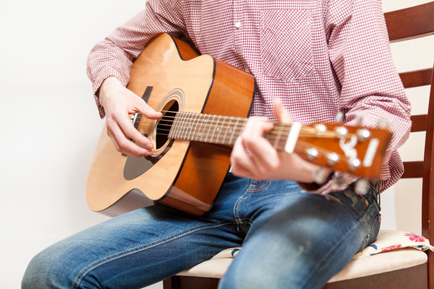 Zdjęcie mężczyzna siedzi na krześle i gra na gitarze akustycznej - Zdjęcie, obraz